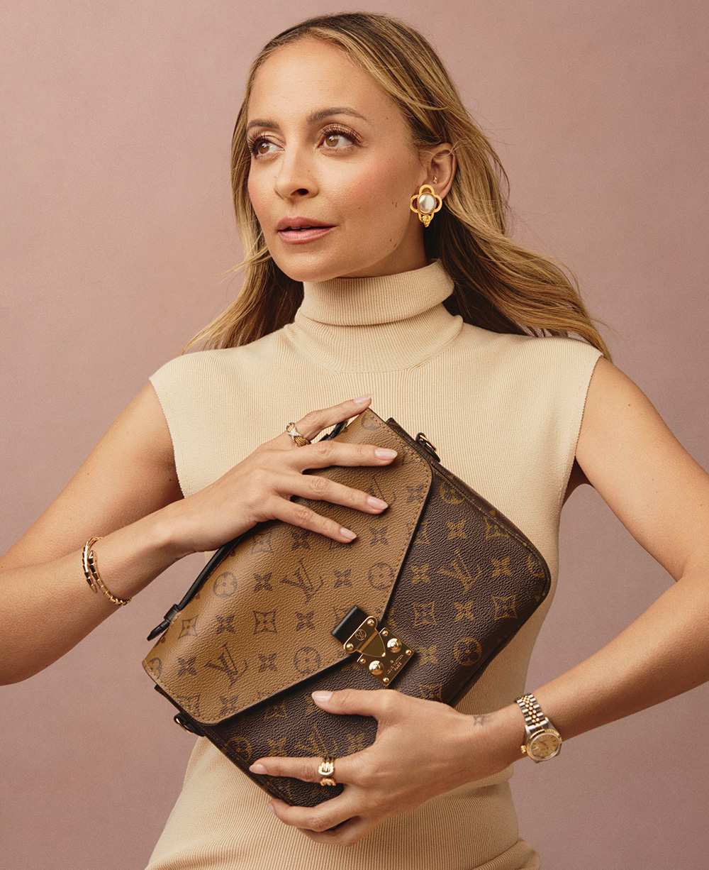 Nicole Richie wearing a beige knit turtlneck sleeveless dress and holding a Louis Vuitton reverse monogram Pochette Metis bag